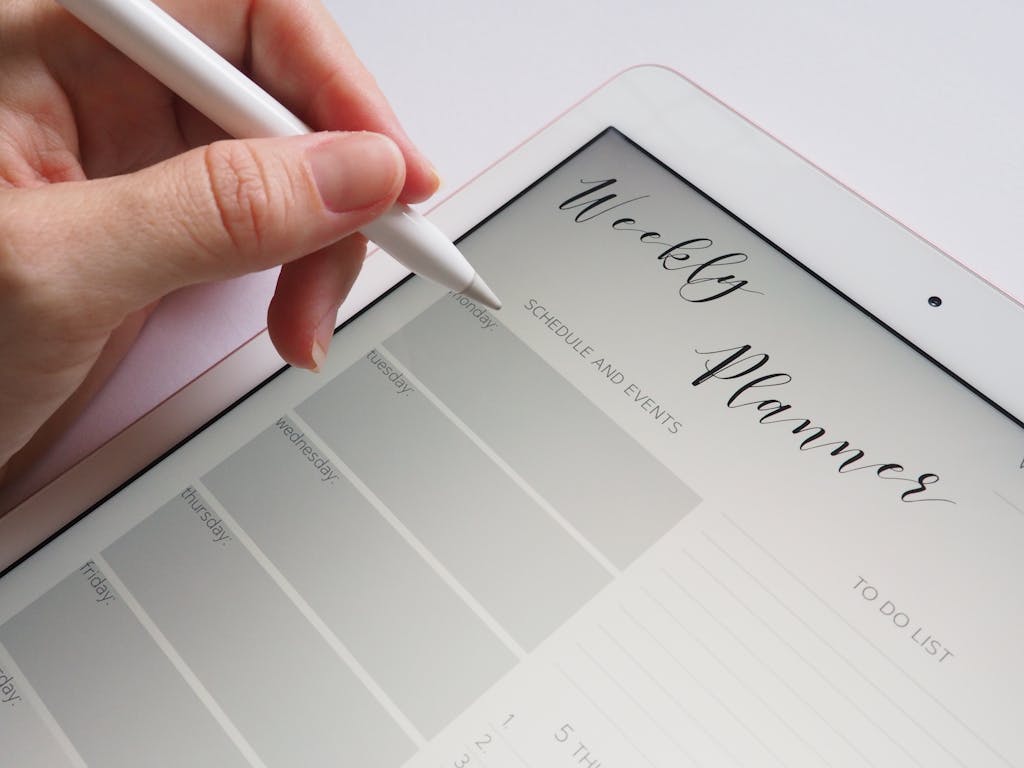 A stylus writing in a digital weekly planner on a tablet screen, ideal for organization.